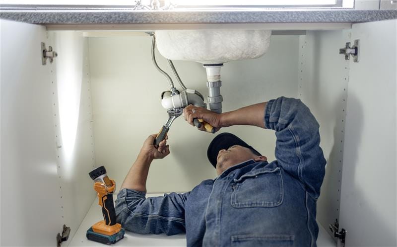 Plumber repairing pipes beneath a bathroom sink in Port Charlotte