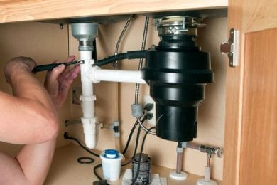 Plumber repairing a garbage disposal beneath a kitchen sink in Port Charlotte