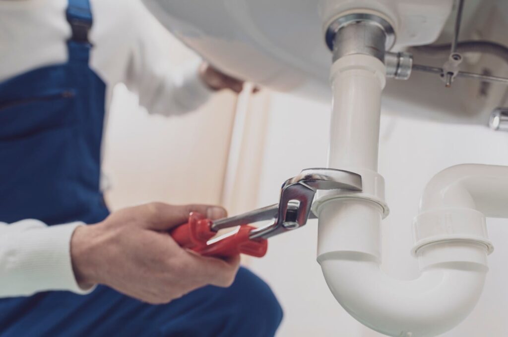 Plumber repairing a white drain pipe beneath a sink in Port Charlotte