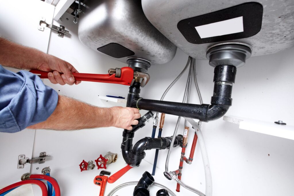 Plumber repairing drain pipes beneath a kitchen sink in Port Charlotte